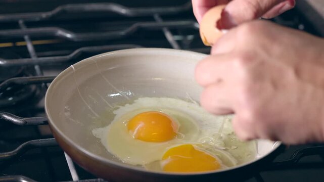 Cracking eggs into a frying pan and cleaning out broken shells with finegrs