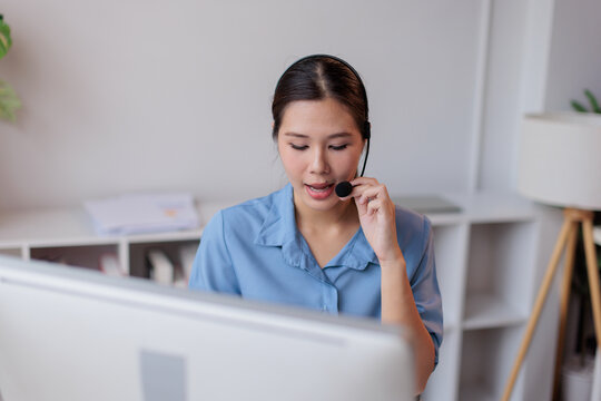 Asian woman operator wearing a headset with microphone talking to customer, providing telemarketing support, online assistance, and virtual help in a modern office environment