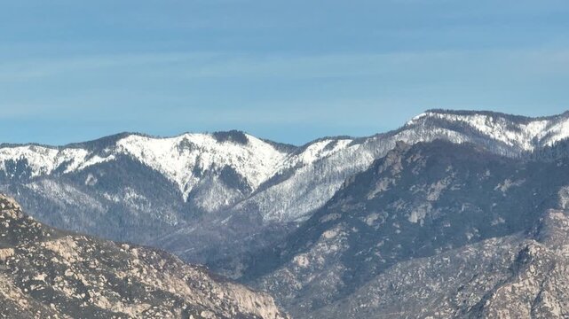 Aerial view of forested mountains with patches of winter snow under a cloudy sky in California
