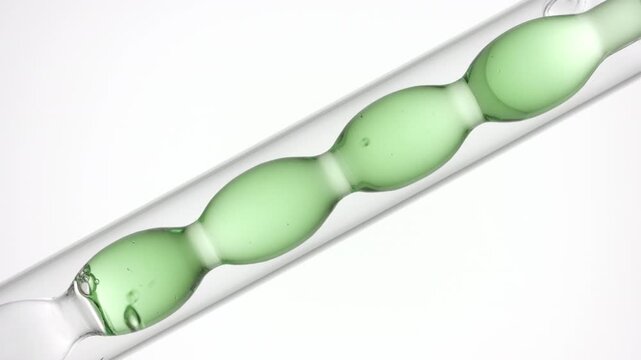 Air bubbles move rapidly through pale transparent green liquid as it fills and drains from a bulb lab condenser on bright white bg | Borage flower hydrosol cosmetic formulation design concept