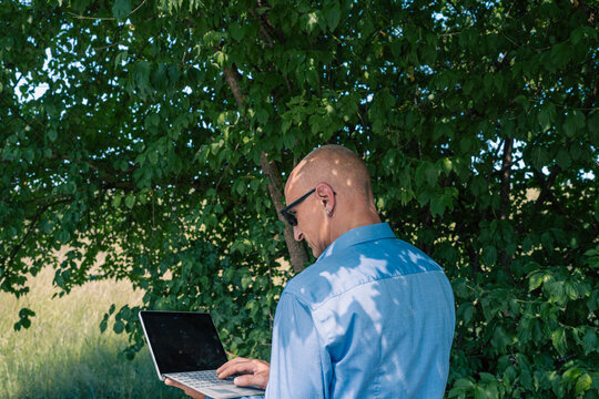 a modern businessman working on a laptop computer under green trees outdoors, conceptual image for remote work and digital nomad lifestyle