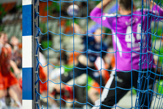 Handball goalpost and blurred goalkeeper and forward during indoor match with blurred players, capturing sports action and competitive atmosphere