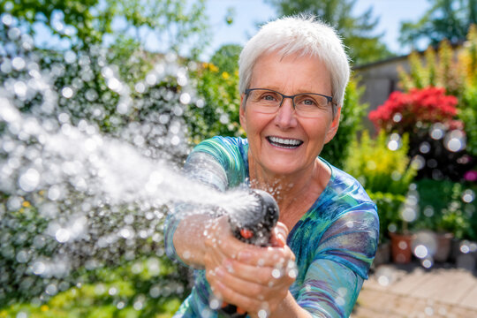 Seniorin mit Wasserschlauch im Garten