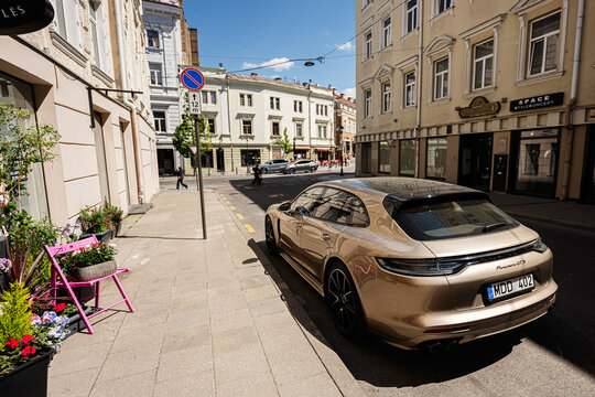 Luxury Porsche Panamera GTS sports car parked on a sunny Vilnius street in Lithuania with city buildings and floral sidewalk seating
