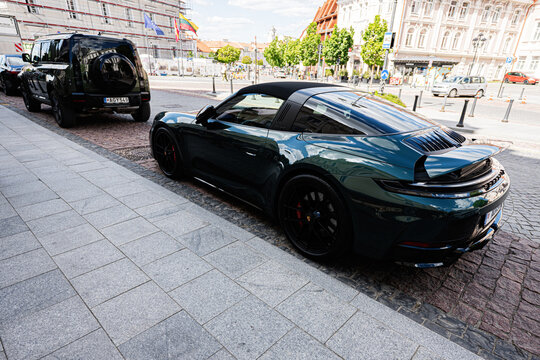 Dark green Porsche 911 Targa 4 GTS sports car parked on a cobblestone street in Vilnius, Lithuania with reflections of city buildings