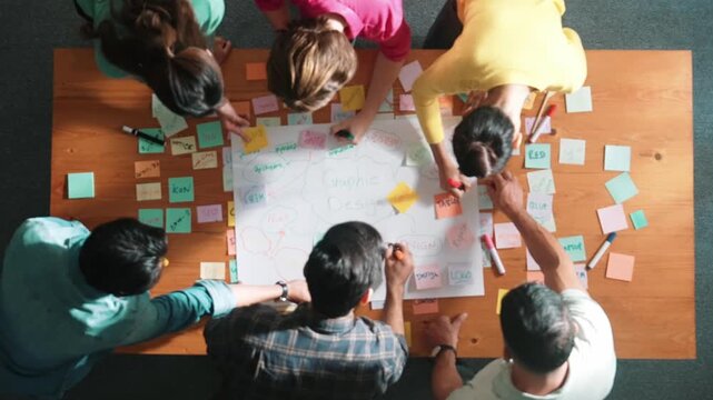 Top view of project manager writing and sticking stick notes. Aerial view of professional business people working together planning strategy while drafting mind mapping at meeting room. Symposium.