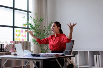 Obraz premium Overwhelmed businesswoman expressing intense anger and stress. Raising arms and screaming as papers fly around her desk in a chaotic office. Depicting burnout. Work pressure