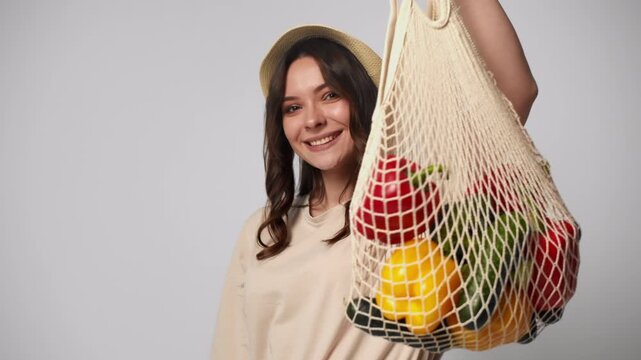 Cheerful woman holding reusable shopping bag with fresh organic vegetables for healthy eating and zero waste lifestyle