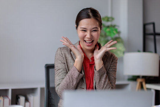 Happy asian businesswoman receiving exciting news on laptop, celebrating achievement and career success with an expressive, joyful reaction in modern office