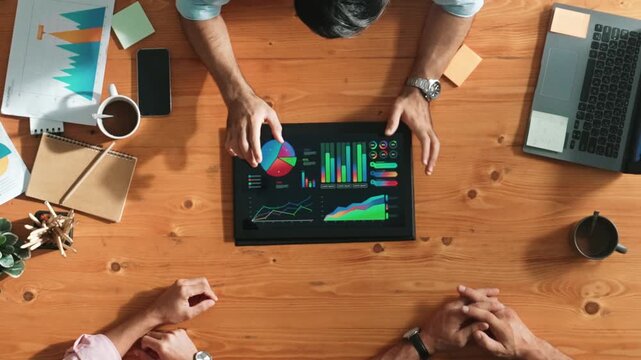 Top aerial view of business man present financial graph to group of smart investors. Professional male leader analyze graph and explain marketing idea by using tablet on meeting table. Convocation.