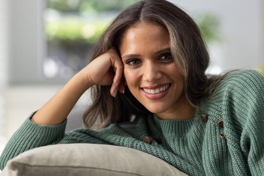 African woman reclining at home, resting head on right hand on sofa cushion, wearing green sweater