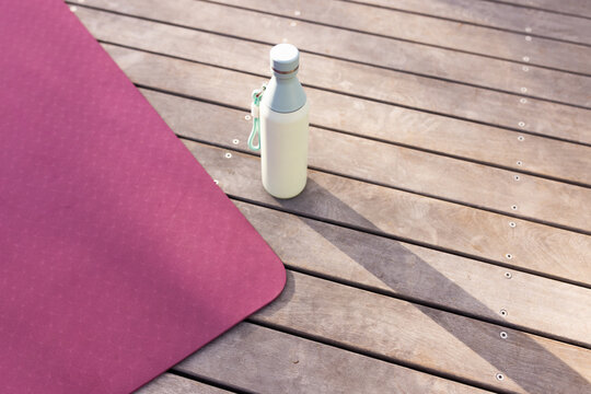 Magenta mat is resting on wooden deck, cream bottle is casting long shadow with mint strap