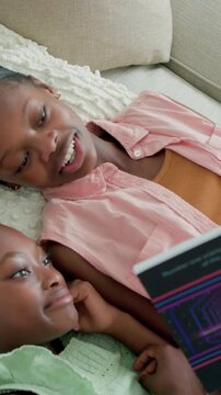 Vertical video: Starting teen reading neon book on couch, wearing pink top, amusing child