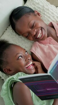 Vertical video: Opening book sisters sharing story on sofa pillow in pink and green laughing