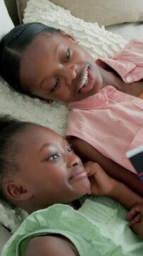 Vertical video: Reading teen in pink top from bright book on couch, child in green dress laughing