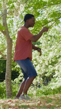 Vertical video: Dancing man in orange tee shifting, woman coming, joining playful dance under tree