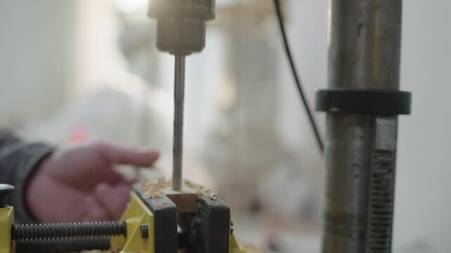 Craftsman drills wood using a workshop vise during carpentry and woodworking process in a light-filled space