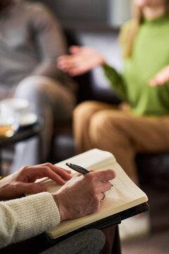 Vertical shot of adult couple attending therapy session, female therapist taking notes while woman speaking, conveying relationship counseling and mental health support