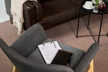 Naklejka premium High angle view of counseling office chair holding intake form and notebook, suggesting adult couple therapy session and mental health support. Useful for psychotherapy marketing and wellness content