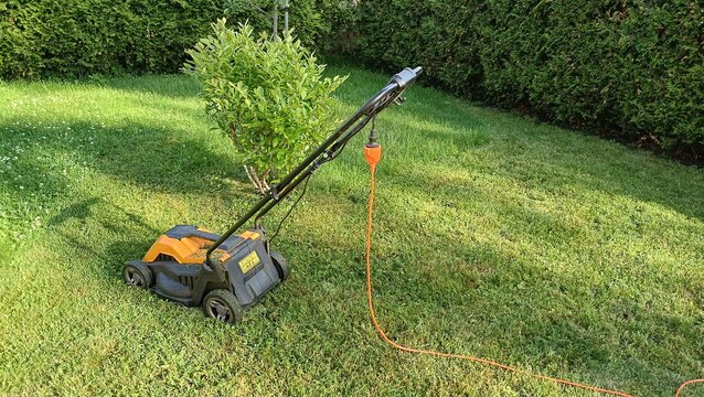 Mowing the grass. Eco electric lawn mower with orange cord on green grass in garden. Sustainable lawn care equipment on backyard lawn.
