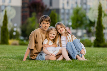 Fototapeta premium three children sitting on a lawn in the summer, in front of a residential complex in a city park