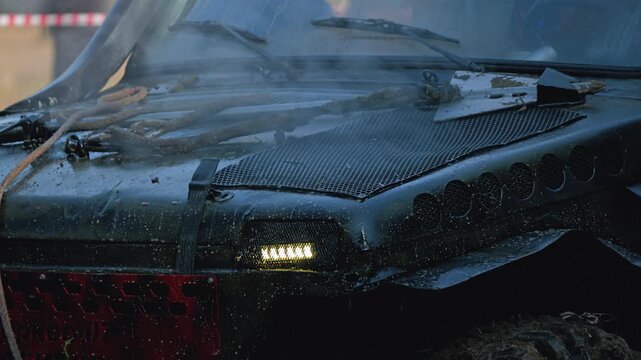 A rugged SUV covered in mud. A hot engine smokes during an extreme rally. The co-pilot tucks a dirty winch cable in front of the hood. Motorsport, power, and adventure