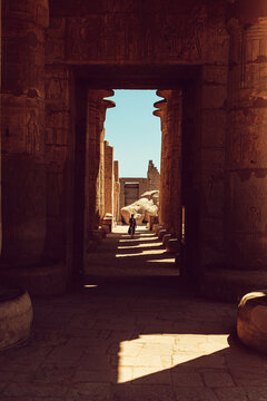 Luxor, Egypt - 04 March 2020: View of a person walking through the monumental stone columns and hieroglyph-covered walls of the ancient Karnak Temple Complex under bright sunlight.