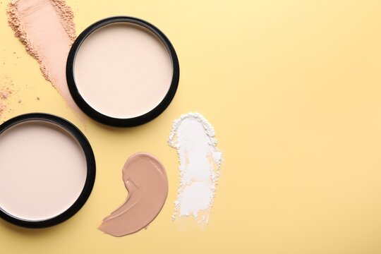 Face powders and liquid foundation on pale yellow background, flat lay. Space for text
