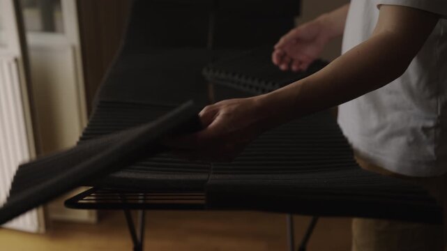 Cropped shot of person placing wet, black acoustic foam panels on metal drying rack after washing, necessary maintenance step for sound absorption studio equipment, close-up, slow motion.
