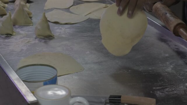 close-up view of hands rolling and shaping dough pieces for making samosas. the image shows the traditional preparation process of forming samosa shells before adding filling and frying