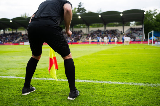 Assistant referee standing on the touchline during a football match, watching play unfold in a crowded stadium