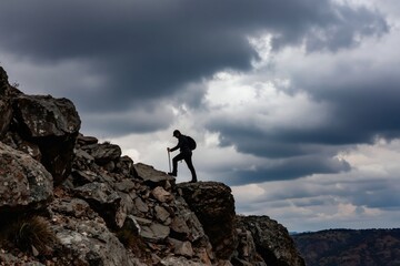 Obraz premium Man hikes up rocky mountain with walking sticks under cloudy sky. Person climbs steep terrain, carries backpack, explores nature wilderness. Dramatic storm clouds gather above summit.