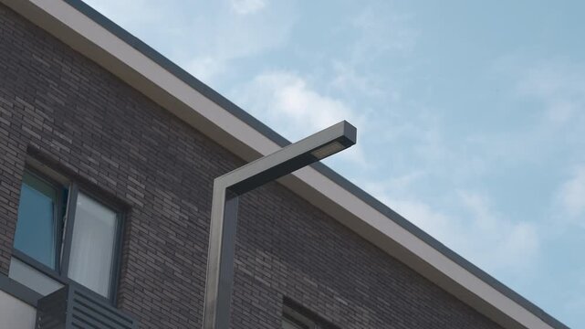 Modern brick residential house with streetlamp against blue sky and soft clouds