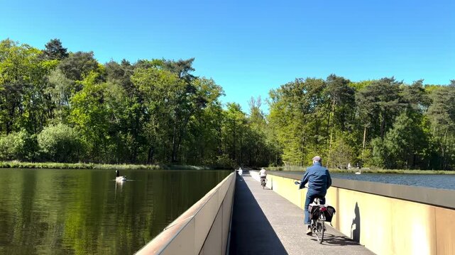 Cyclists on the famous water bike path at Cycling Through Water in Bokrijk, where riders pedal between the waters of a scenic lake. 
