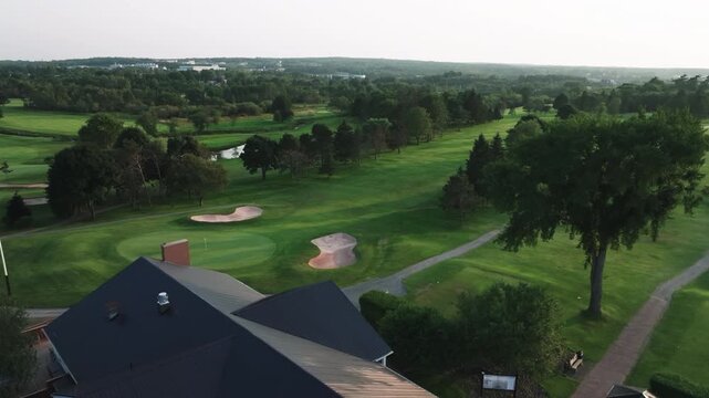 Ascending aerial drone shot revealing the roof of a golf course clubhouse before rising to showcase the surrounding golf course in Truro, Nova Scotia, Canada. Cinematic footage featuring green