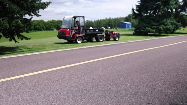 Big professional riding lawn mower with an operator on it driving in city park in sunny summer day.