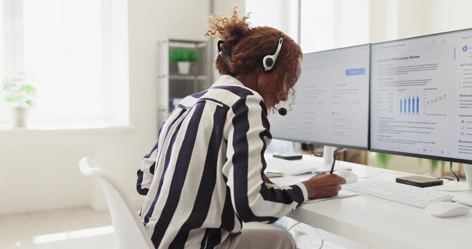 Woman operator with headset microphone answers customer call. She works at a computer in a bright office, providing reliable support and service for clients. Clear concept of smart support.