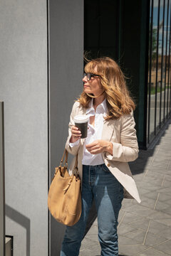 Mature businesswoman with takeaway coffee walking outside a modern office building