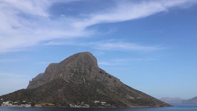 Scenic coastal view of Telendos, a picturesque island in the southeastern Aegean Sea near Kalymnos. The landscape features dramatic limestone cliffs rising above crystal-clear turquoise waters,