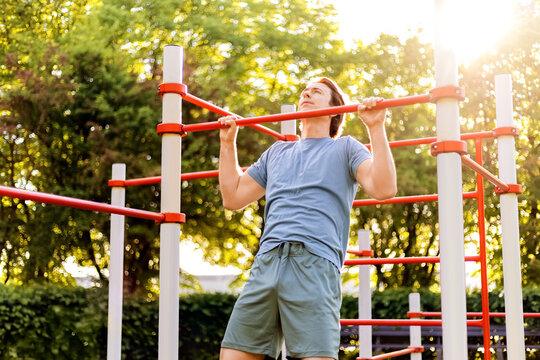 Man doing pullups on outdoor calisthenics bars during a fitness workout in a sunny park. Athlete training bodyweight exercise.