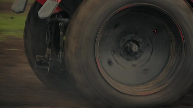 Closeup of large tractor wheels spinning rapidly on dirt track, kicking up dust mud during competitive event. The speed and power of a racing tractor. Slow motion
