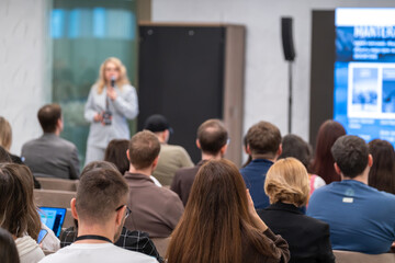 Fototapeta premium Business speaker presenting to engaged audience during conference, attendees listening, taking notes, networking in modern meeting room.