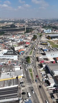 Imagem a&eacute;rea de corredor urbano com fluxo de ve&iacute;culos, empresas, armaz&eacute;ns, resid&ecirc;ncias e vias secund&aacute;rias, mostrando a din&acirc;mica comercial e o crescimento da cidade.
