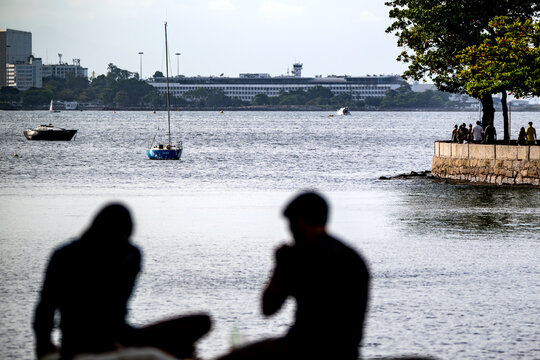 Rio de Janeiro, Brazil - 14 June 2026: View of people sitting at Mureta da Urca overlooking Guanabara Bay with sailboats and the city skyline in the background.