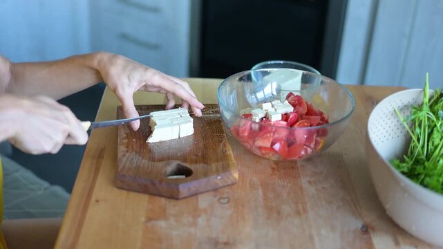 Woman slicing tofu beside bowl of tomatoes and herbs while preparing healthy meal video Full HD