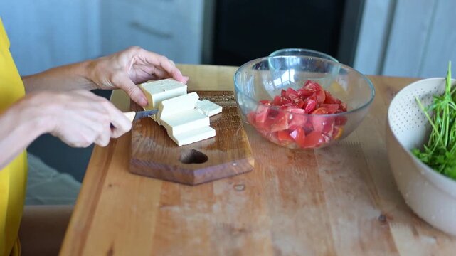 Woman slicing tofu beside bowl of tomatoes and herbs while preparing healthy video Full HD meal