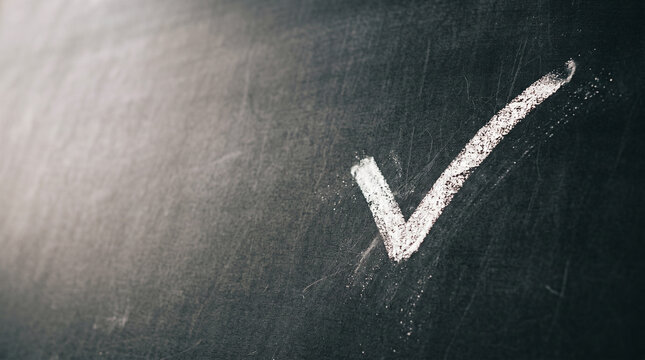 A white chalk check mark drawn on a black chalkboard surface. The drawing is clear and prominent, showcasing a simple yet effective symbol of approval.