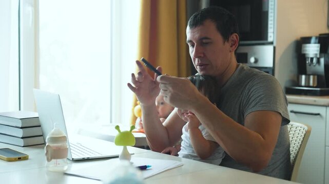 Father multitasks at home, holding baby on lap while talking on phone. Dad works on laptop with infant in arms. Second baby sits in high chair. Parent juggles childcare and remote work.