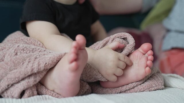 Adorable baby feet wrapped in soft pink textured blanket on comfortable bed showing tiny delicate toes and chubby infant legs. Newborn child resting peacefully in cozy warm nursery bedroom.