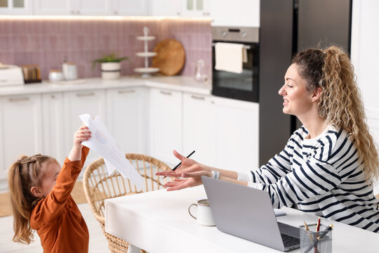 Woman working at white table and her daughter in home office